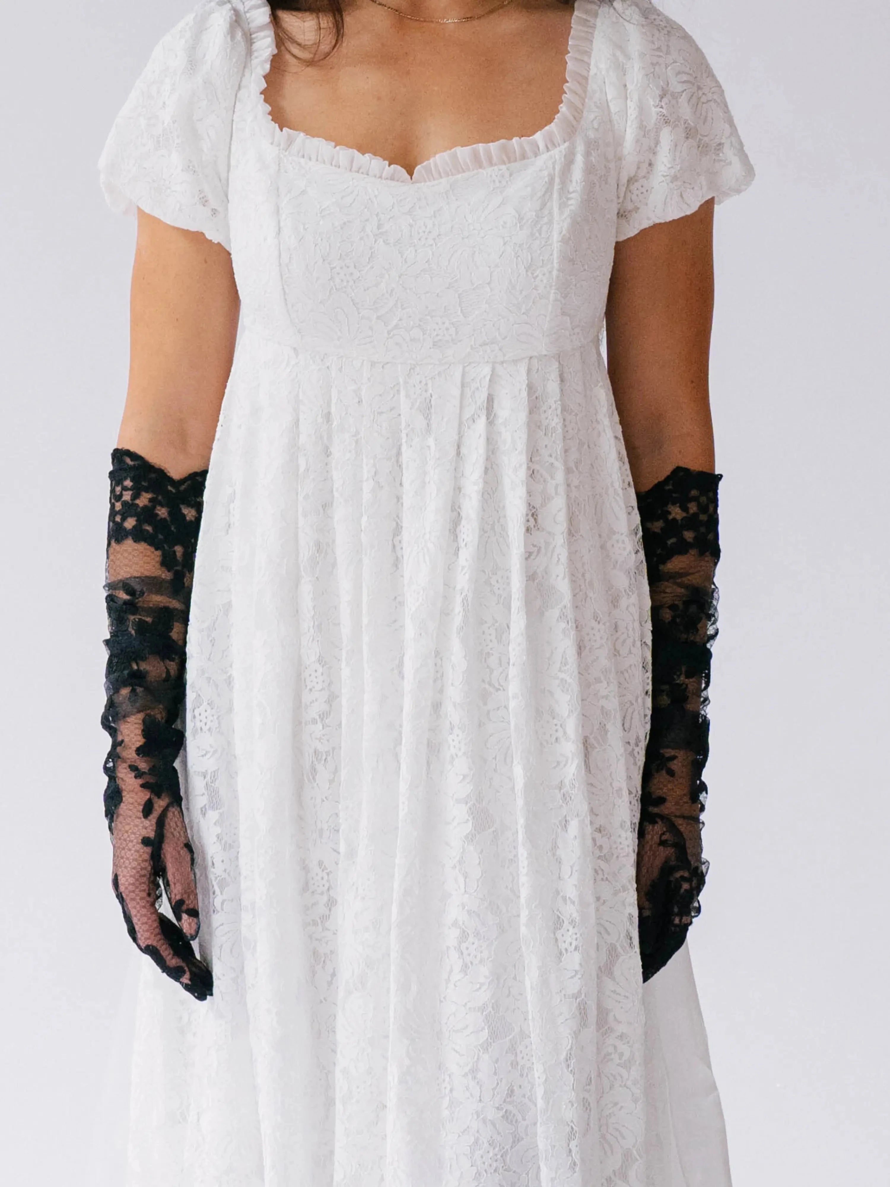 White lace dress with black lace opera gloves on a plain background