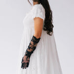 Woman wearing a white dress with black lace opera gloves against a white background