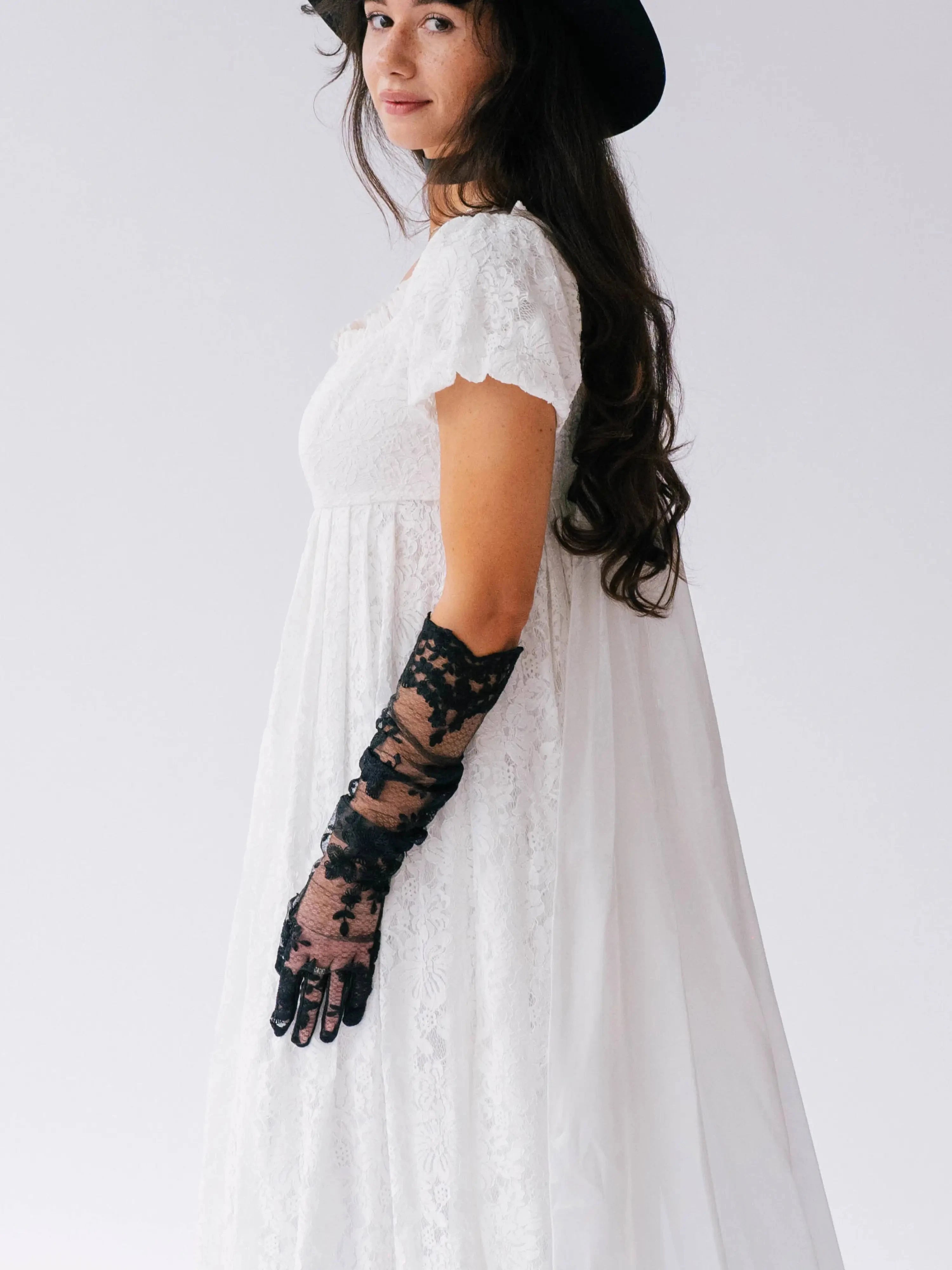 Woman wearing a white dress with black lace opera gloves against a white background