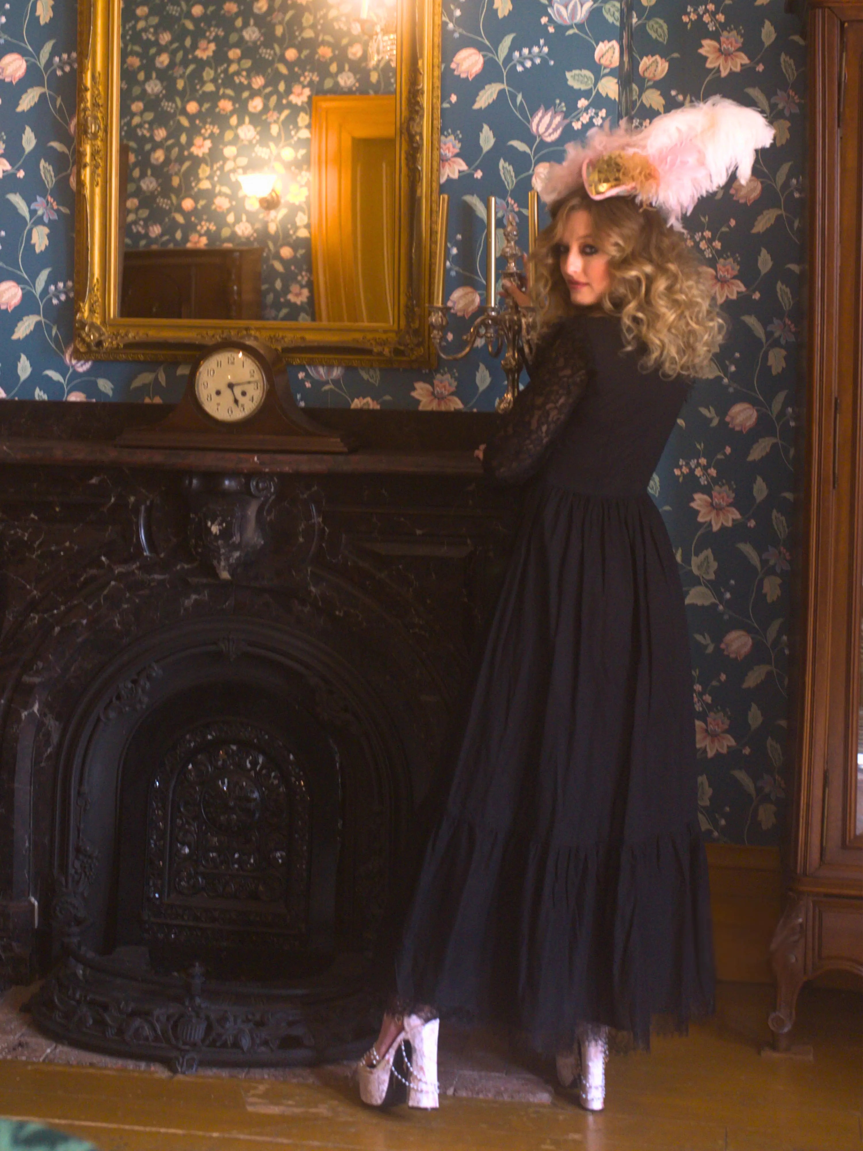 A woman in a black cotton maxi dress is standing in a room with floral wallpaper and a fireplace.
