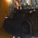 A woman in a black long lace sleeve dress with an antique headpiece is sitting in front of a fireplace.
