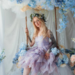 A woman wearing a tulip dress sitting on a swing surrounded by floral arrangements.