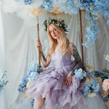 A woman wearing a tulip dress sitting on a swing surrounded by floral arrangements.
