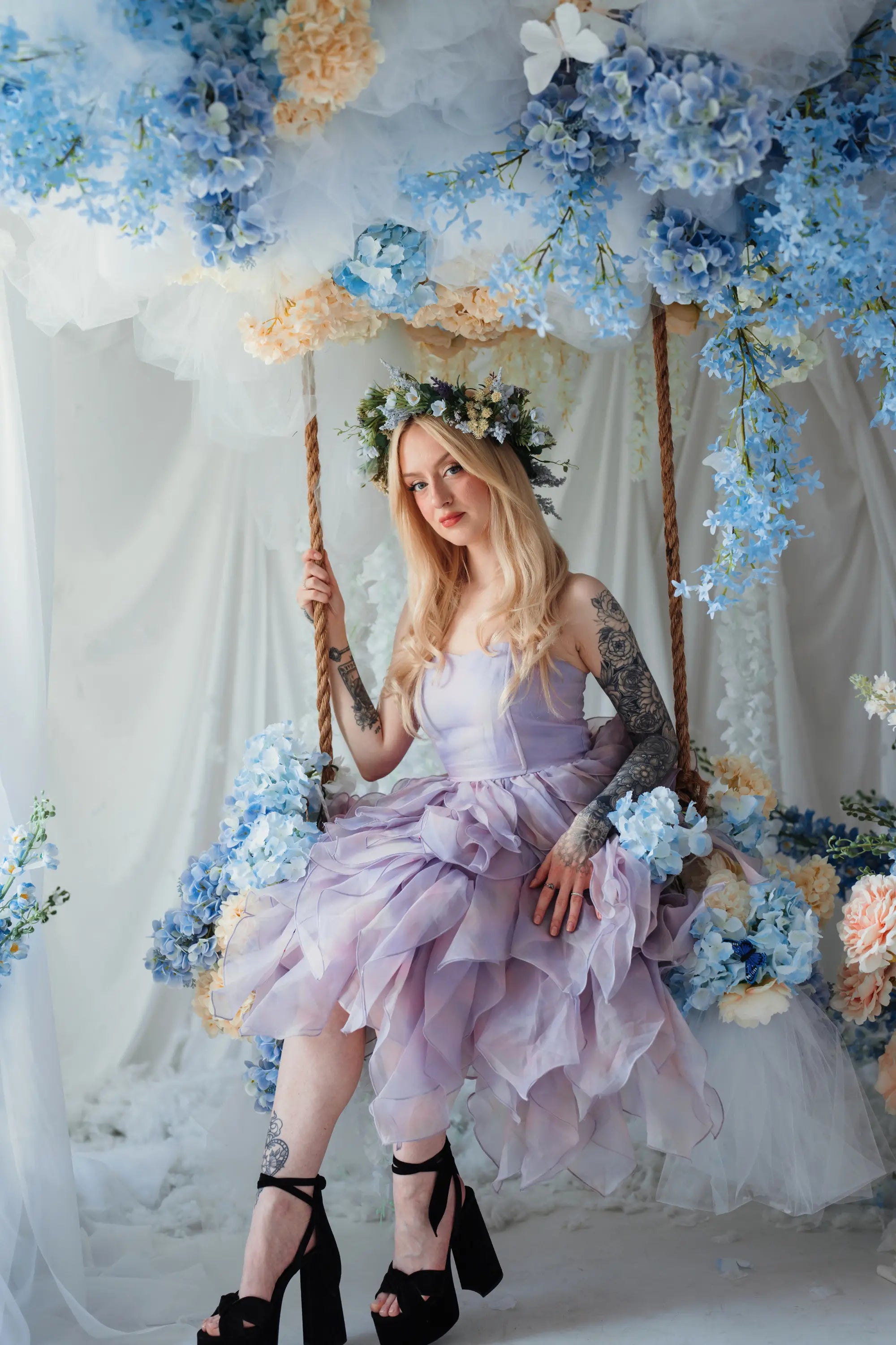 A woman wearing a tulip dress sitting on a swing surrounded by floral arrangements.