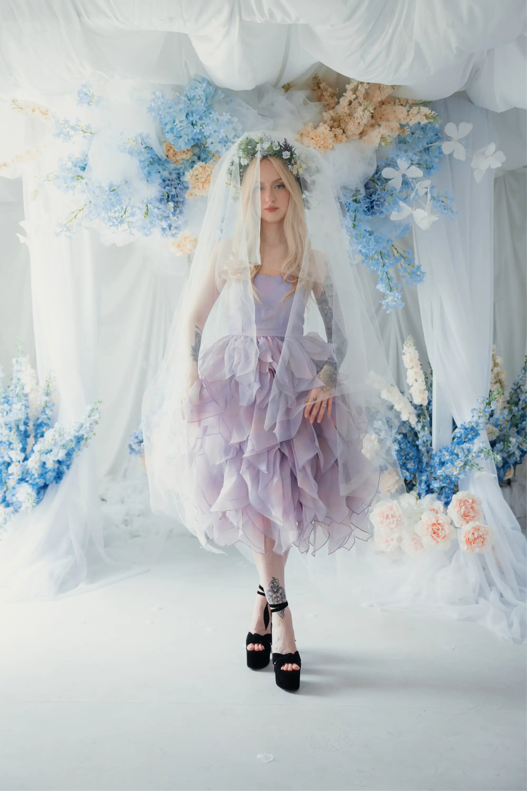 A woman wearing a tulip dress with a white tulle veil surrounded by floral arrangements.