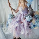 A woman wearing a lavender tulip dress sitting on a swing surrounded by floral arrangements.