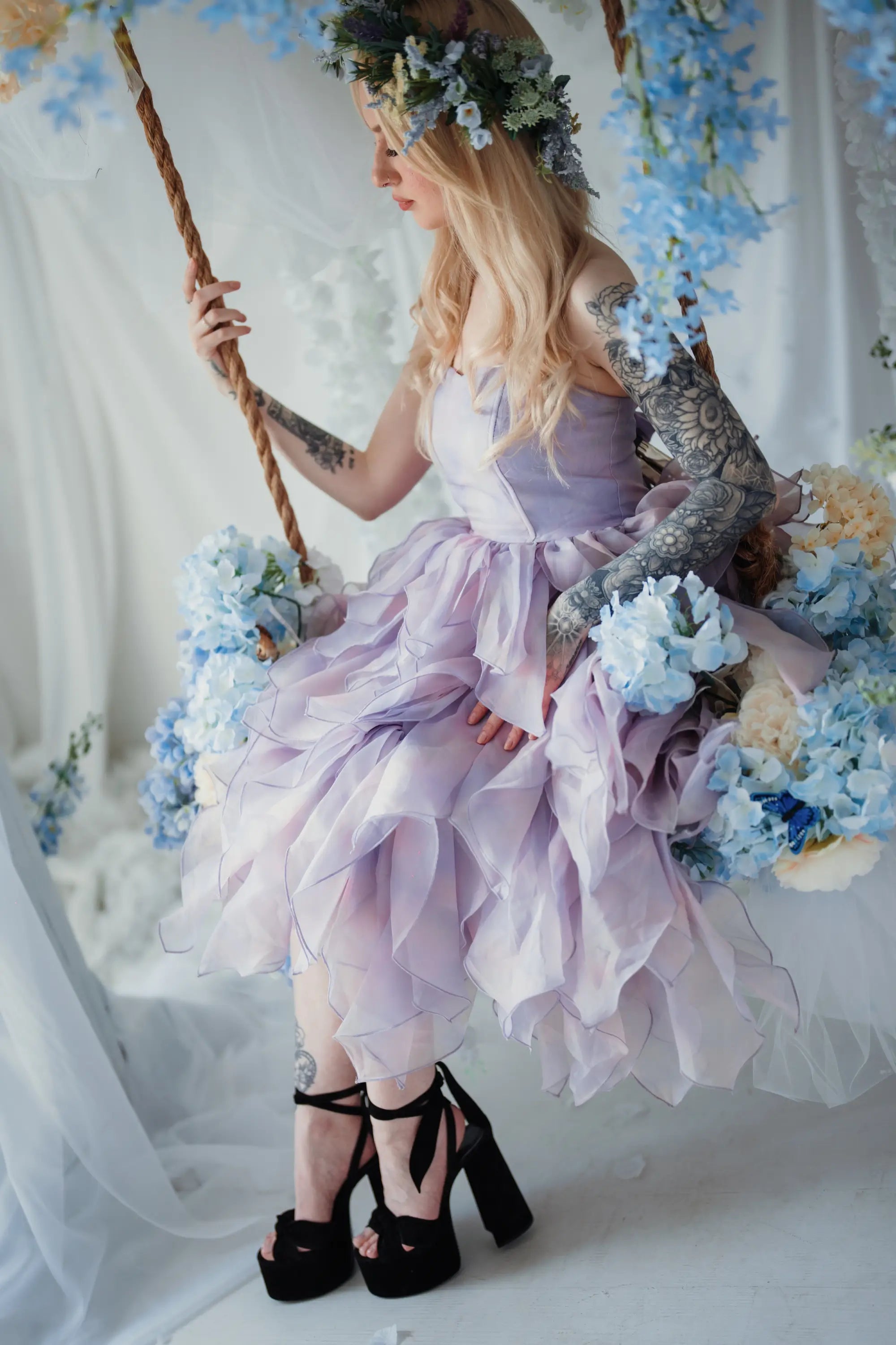 A woman wearing a lavender tulip dress sitting on a swing surrounded by floral arrangements.