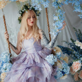 A woman wearing a the Eventyr Tulip Dress sitting on a swing surrounded by floral arrangements.