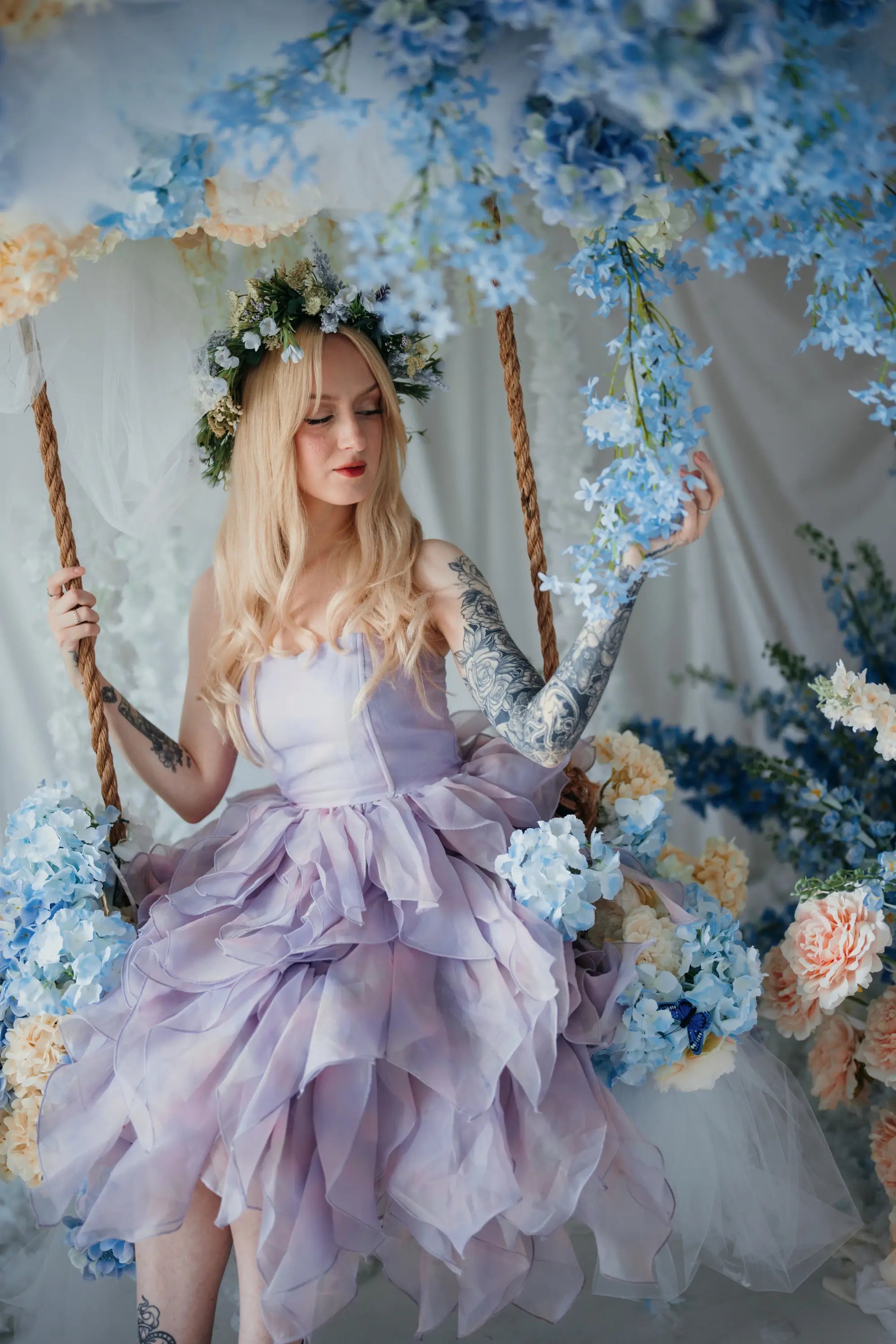 A woman wearing a the Eventyr Tulip Dress sitting on a swing surrounded by floral arrangements.