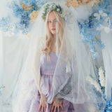 A woman wearing the Eventyr Tulip Dress with a white tulle veil surrounded by floral arrangements.