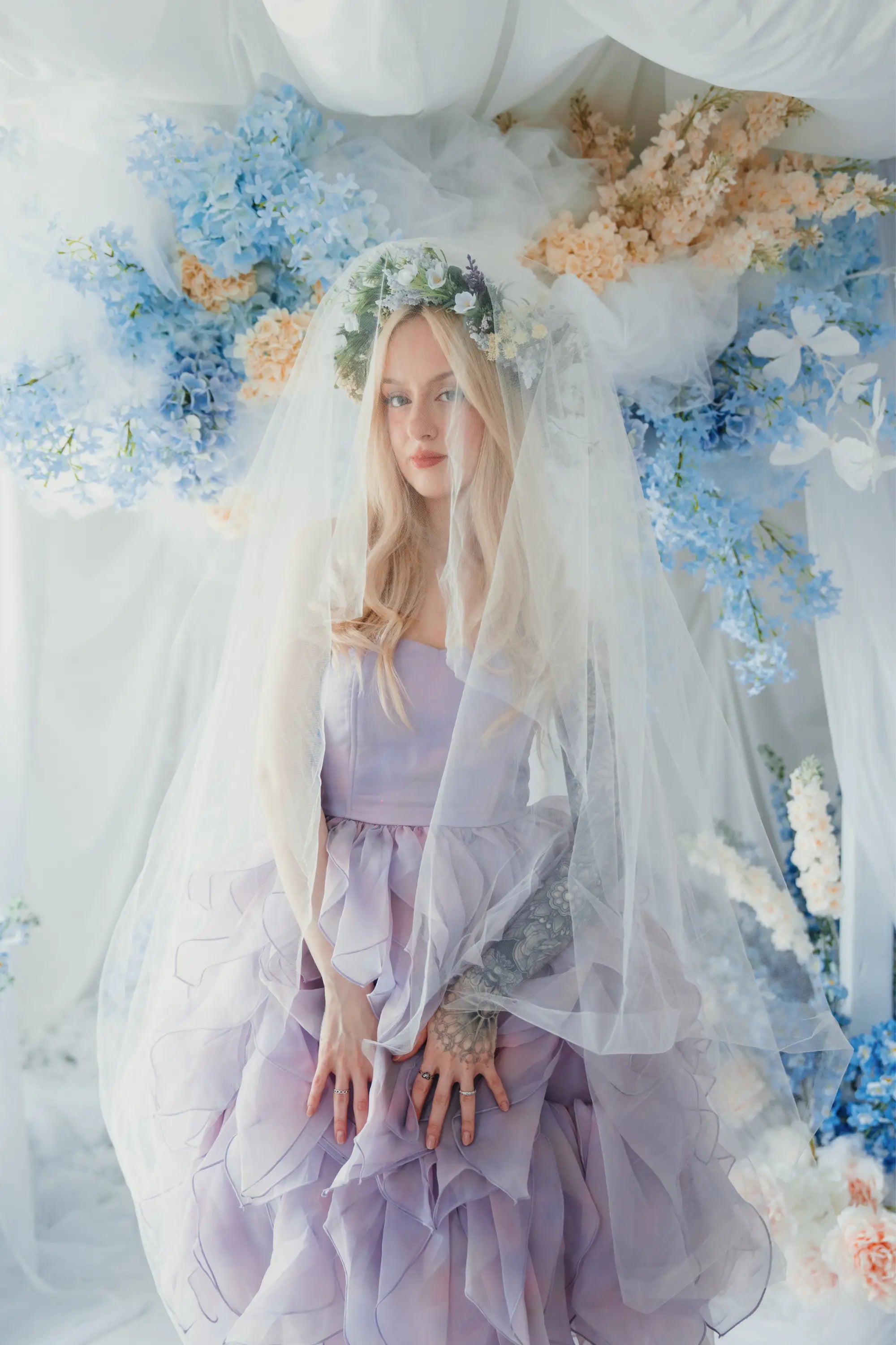 A woman wearing the Eventyr Tulip Dress with a white tulle veil surrounded by floral arrangements.