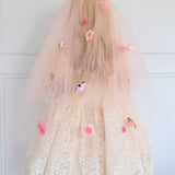 Back view of the Secret Garden Floral Veil featuring layered peach tulle and vibrant pink flowers. Worn by a woman in a white lace dress.