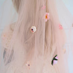 Floral wedding veil with 3D hand sewn decorations worn by a woman.