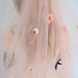 Floral wedding veil with 3D hand sewn decorations worn by a woman.