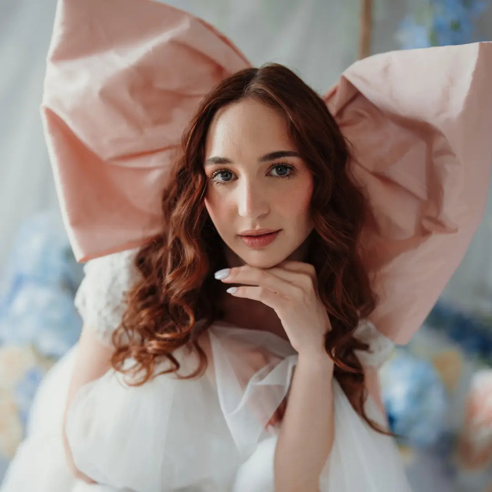 A woman wearing a giant pink hair bow and a white lace maxi dress.