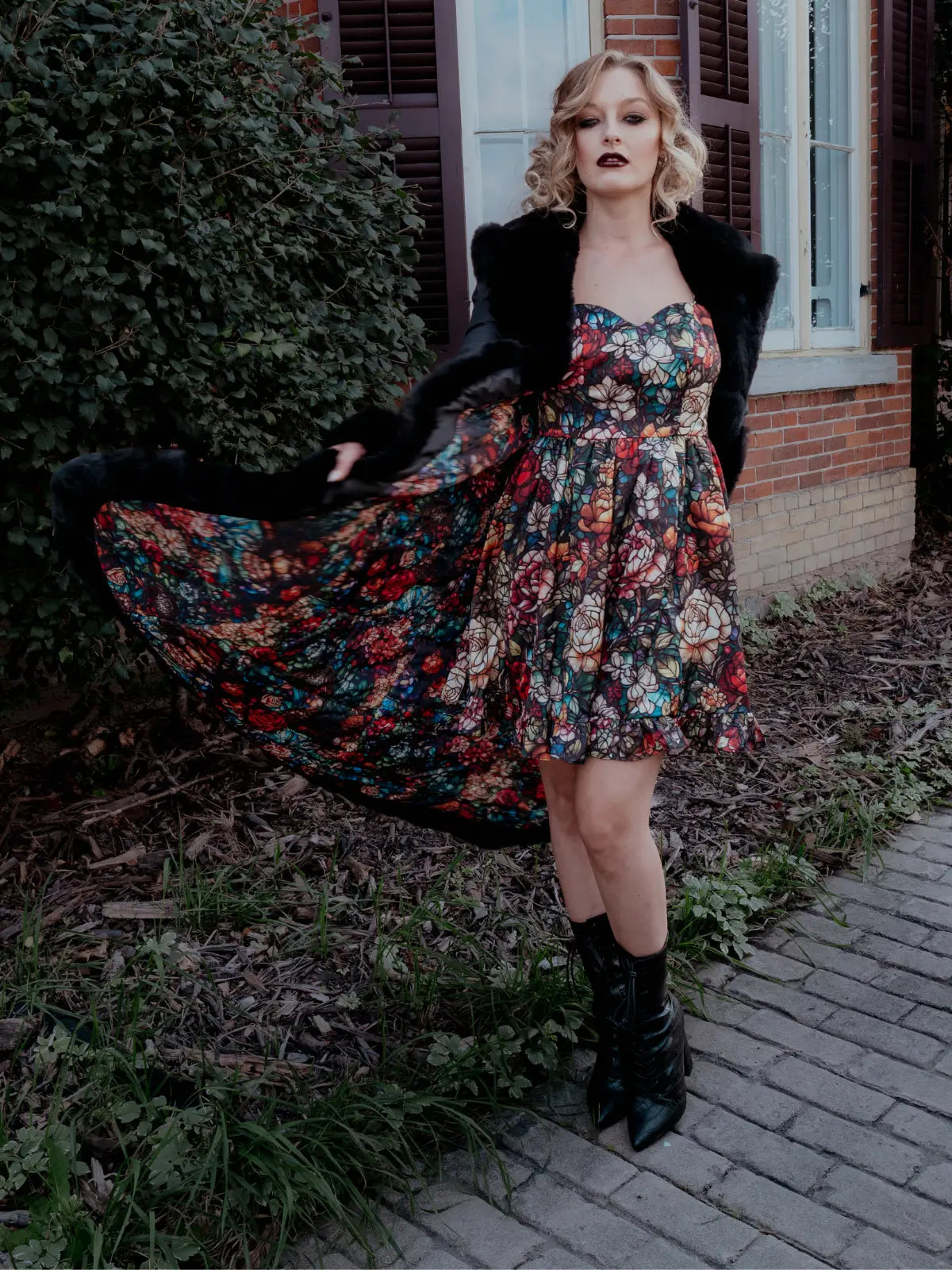 A woman is outdoors, wearing a long black coat and a darling mini dress in an Ivory Sheep stained glass print.