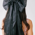 Close-up view of a woman wearing the black swan grand hair bow on their head against a white background.
