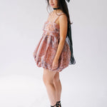 A side view of a woman wearing a floral dress with a black hair bow in her hair on a white background.