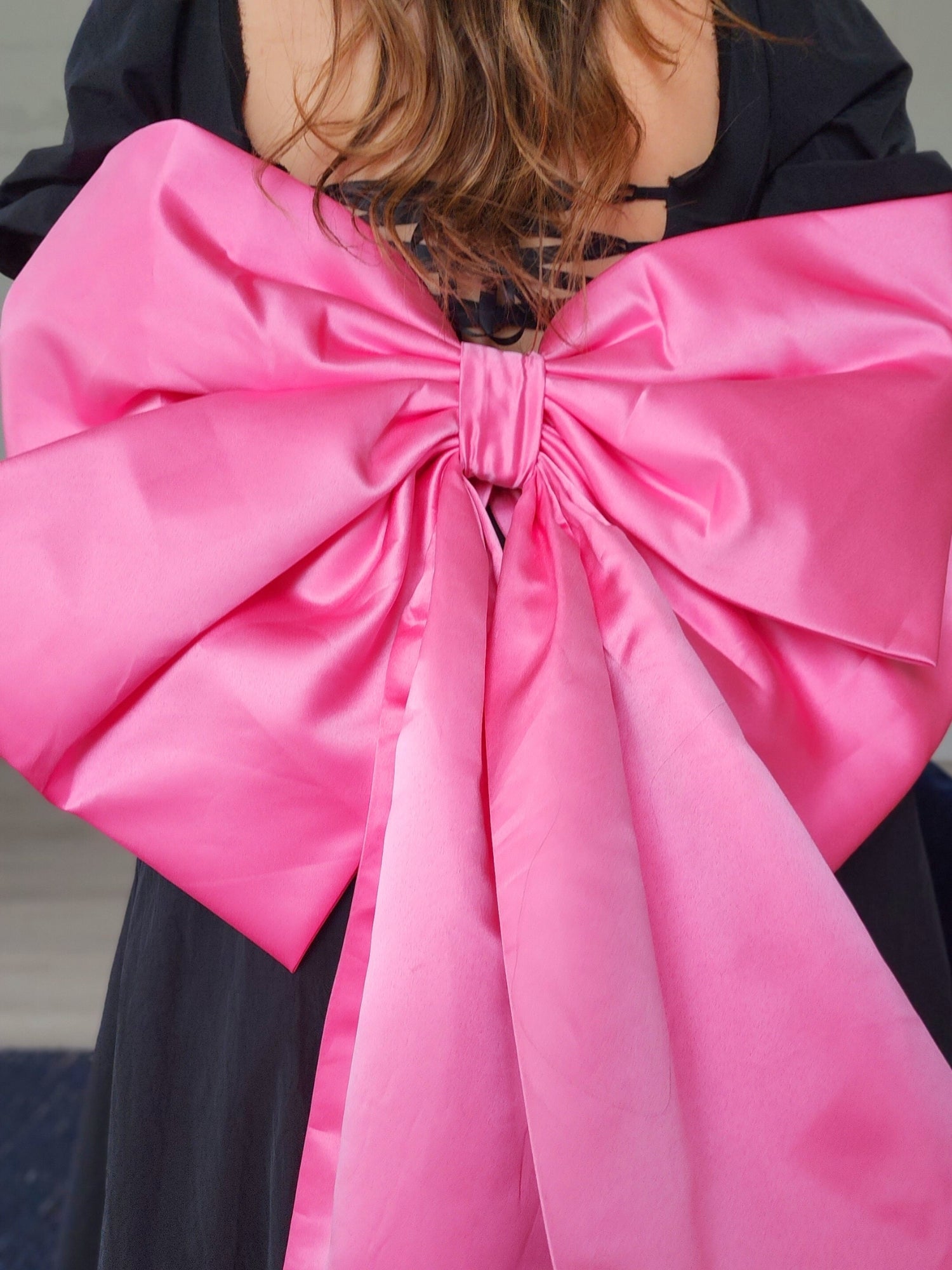 Bright pink satin bow on dark garment for The Grand Bow Sash, perfect for bow lovers