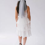 A woman wearing a white bridal mini dress with black lace-up platform shoes, and the Ivory Grand Bridal Hair Bow in her hair, viewed from the back.