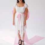 A woman wearing a white lace dress with a large pink bow belt and black platform heels for a statement look.