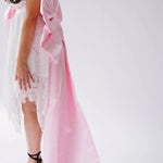 A woman wearing a white lace mini dress featuring the Ballet Pink Grand Bow Belt.