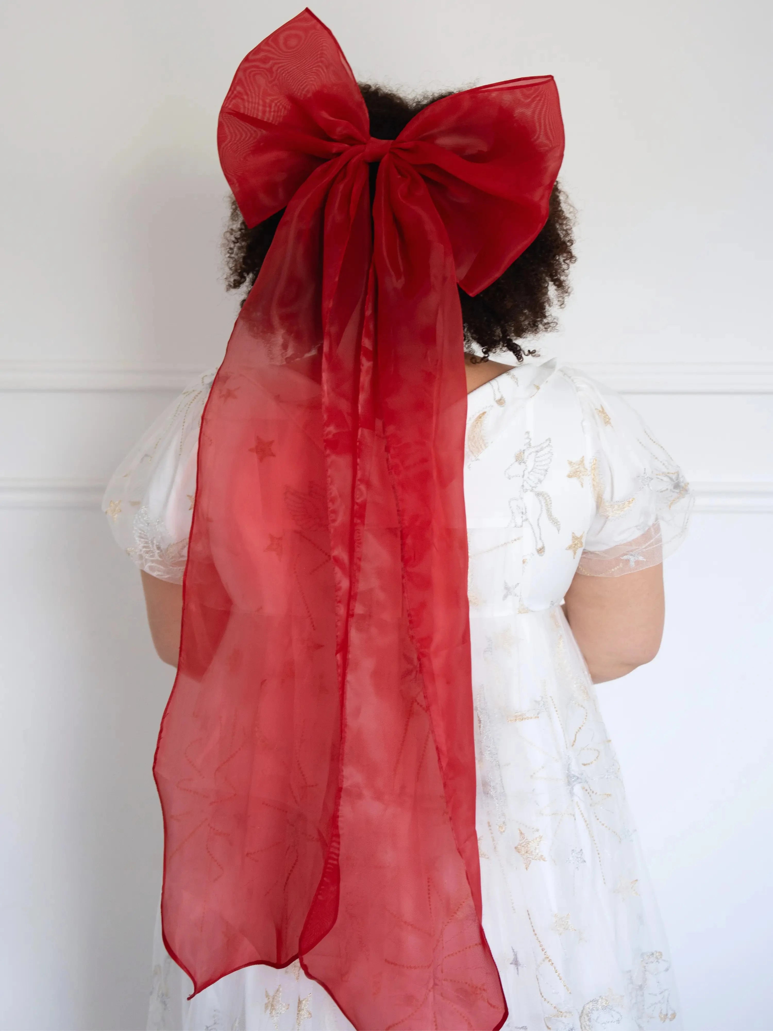 A plus-sized woman wearing a large red hair bow and a lace maxi dress, against a white background.