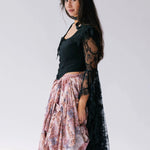 Side view of The Guinevere's Revenge Black Corset Top with dramatic lace sleeves and fitted silhouette, styled with a pink floral skirt.