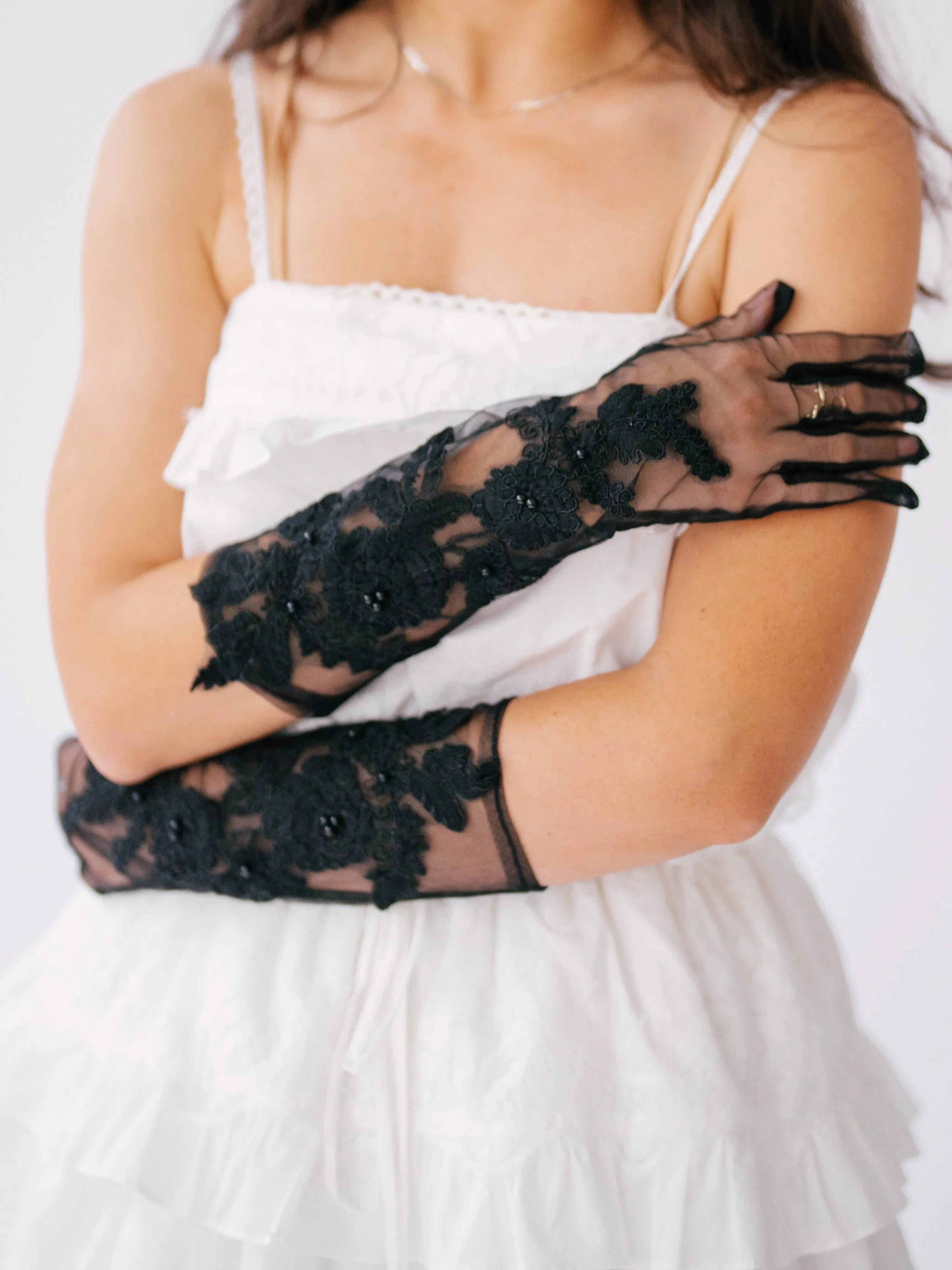 Romantic long black lace gloves with floral embellishments worn with a white mini dress.