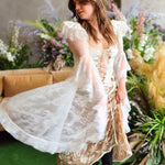 A woman in a flowing white lace corset top surrounded by florals.