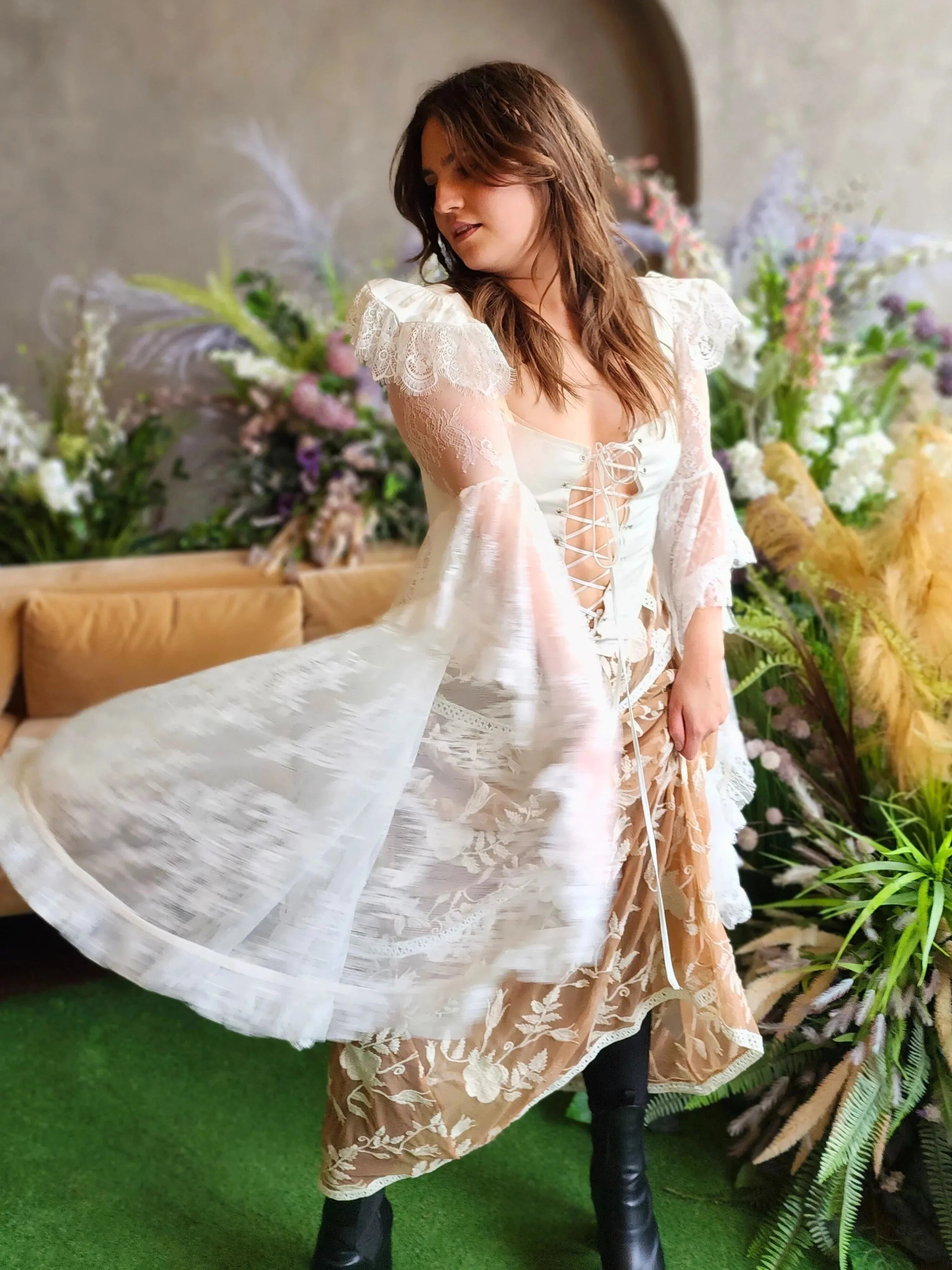A woman in a flowing white lace corset top surrounded by florals.