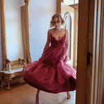 A woman in a red organza midi dress standing in a room with wooden floors and large mirrors.