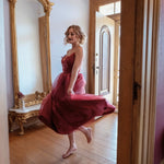 A woman in the Harlow Crimson Organza Midi Dress is standing in a room with wooden floors and an ornate mirror.
