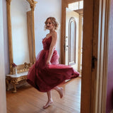 A woman in the Harlow Crimson Organza Midi Dress is standing in a room with wooden floors and an ornate mirror.