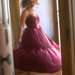 A woman in a red organza midi dress is standing in a doorway.