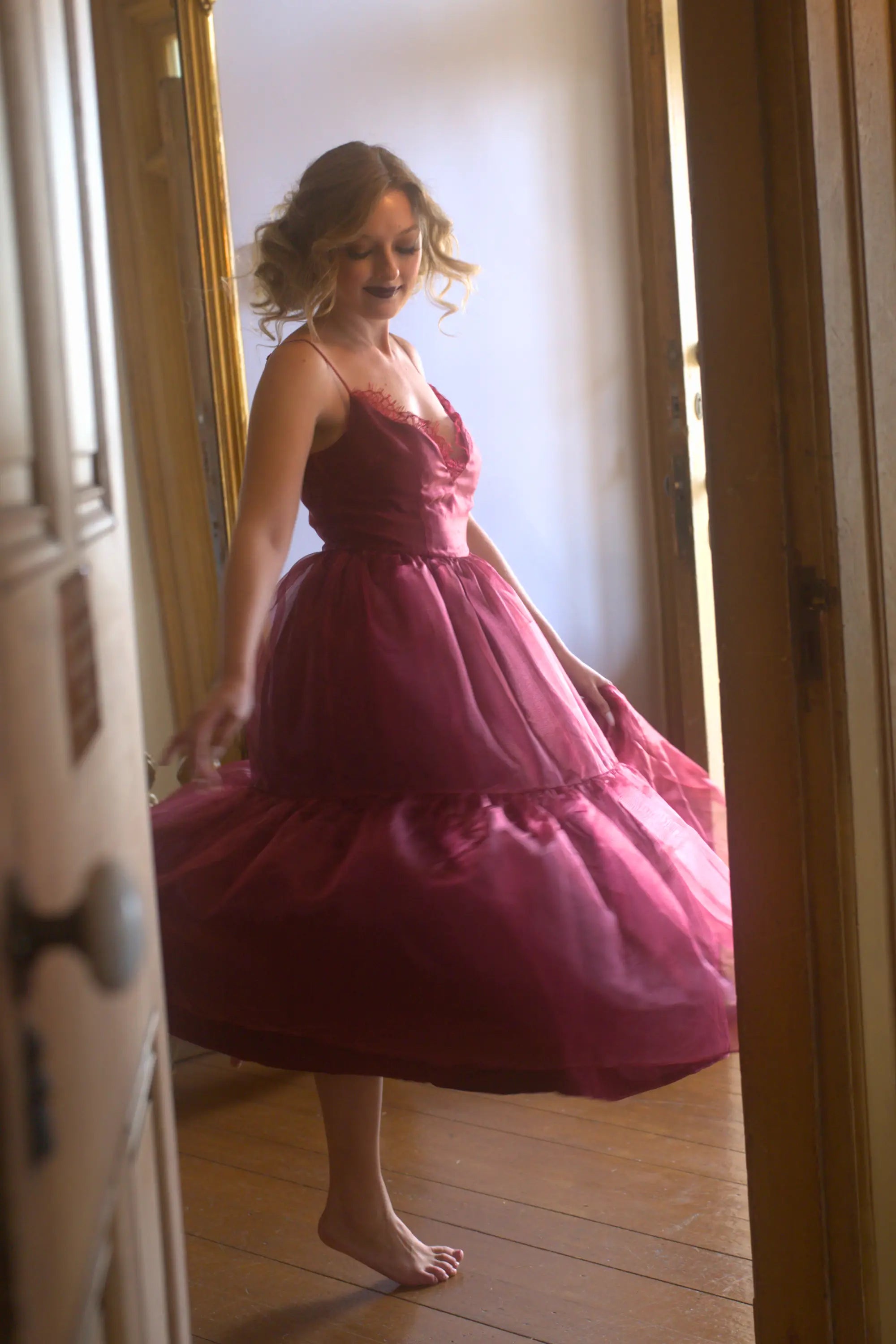 A woman in a red organza midi dress is standing in a doorway.
