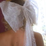 A close-up of the heirloom white lace grand hair bow worn by a person, with a blurred background.