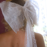 A close-up of the heirloom white lace grand hair bow worn by a person, with a blurred background.