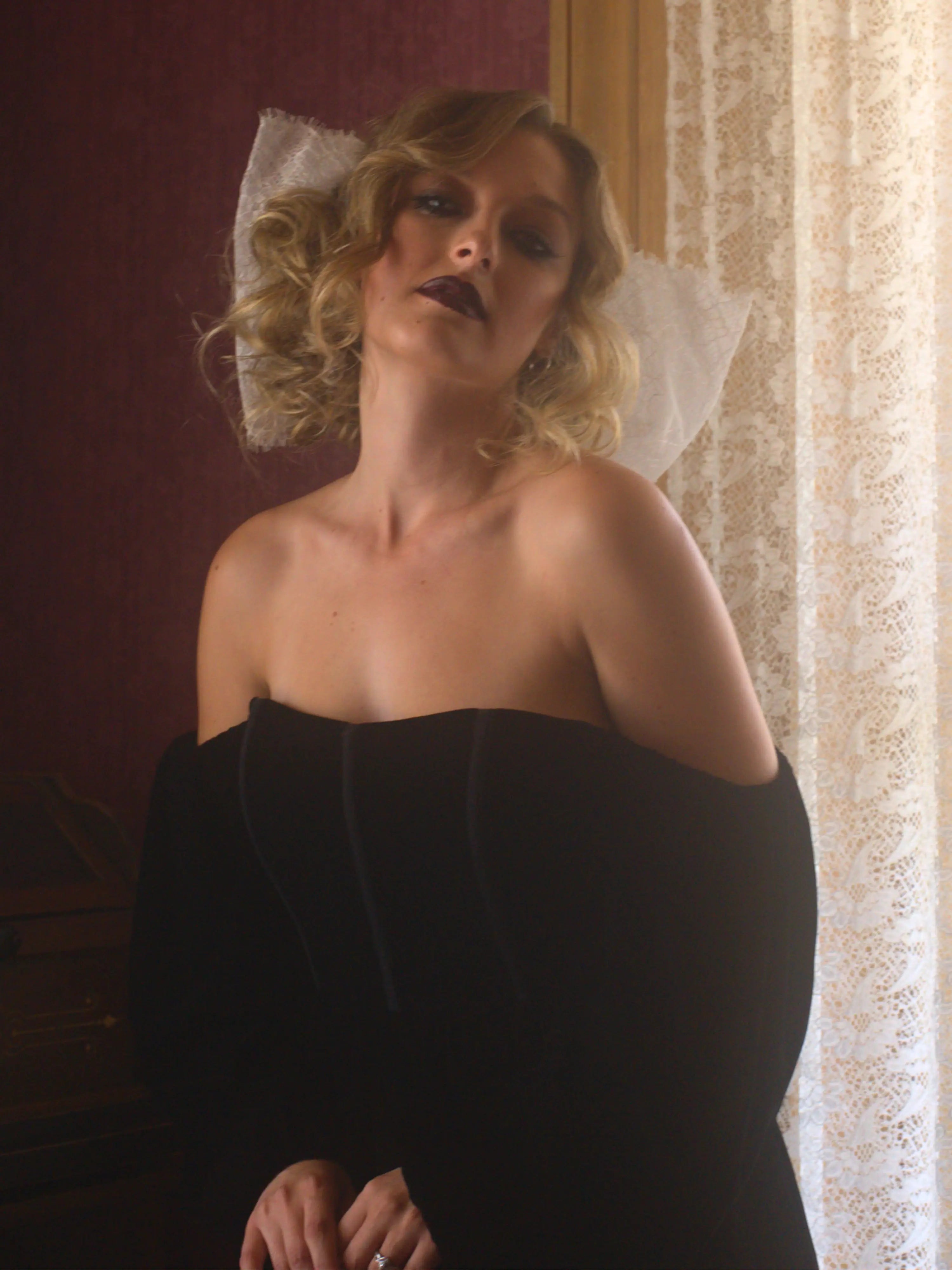 A woman wearing a black strapless velvet mini dress and a white lace hair bow.