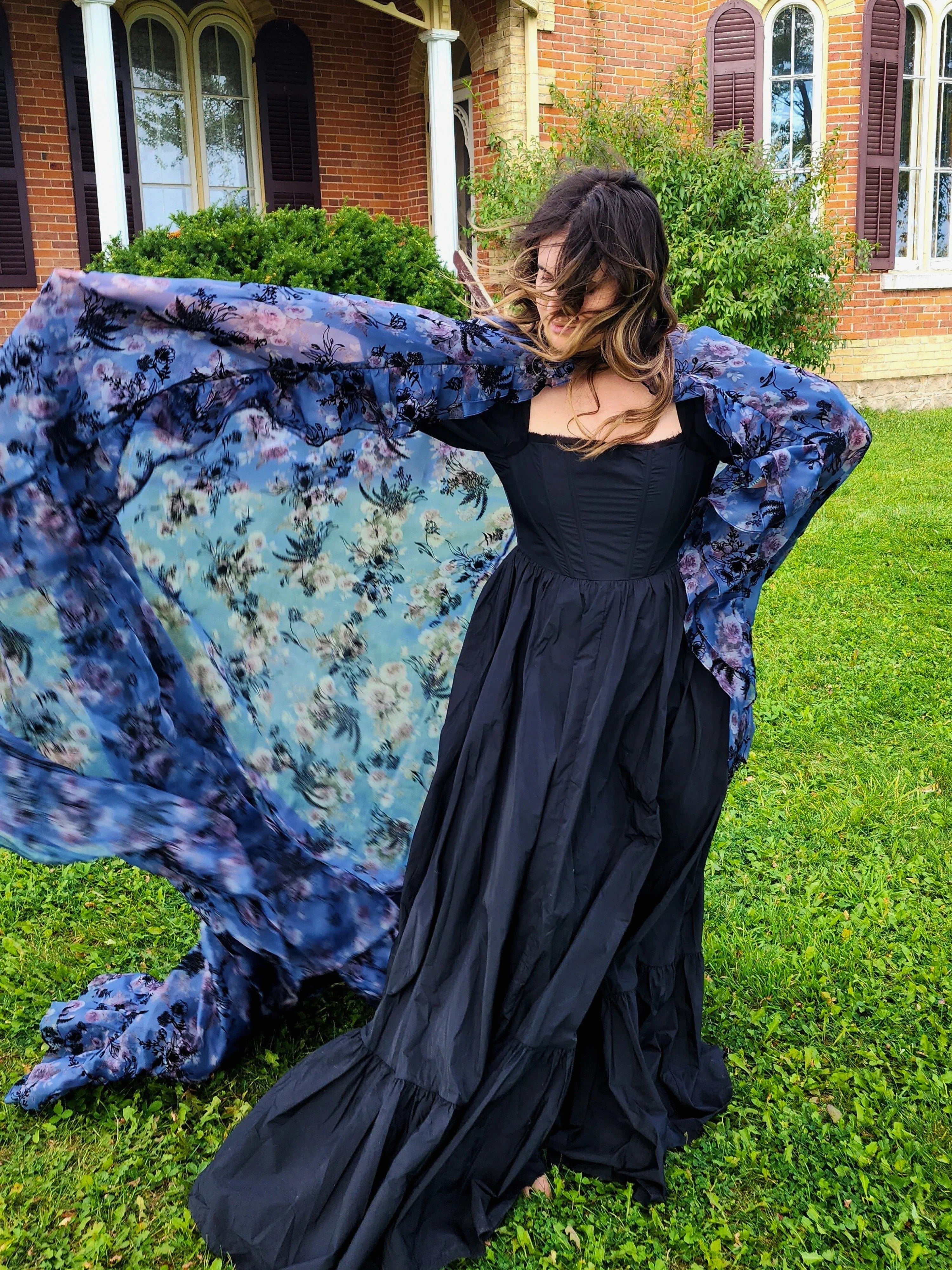 Woman in a flowing black dress showcasing the High Priestess Cape with a blue shawl