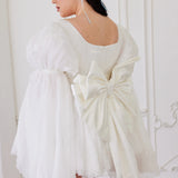 White dress with a grand bow sash and flared sleeves exuding whimsical elegance