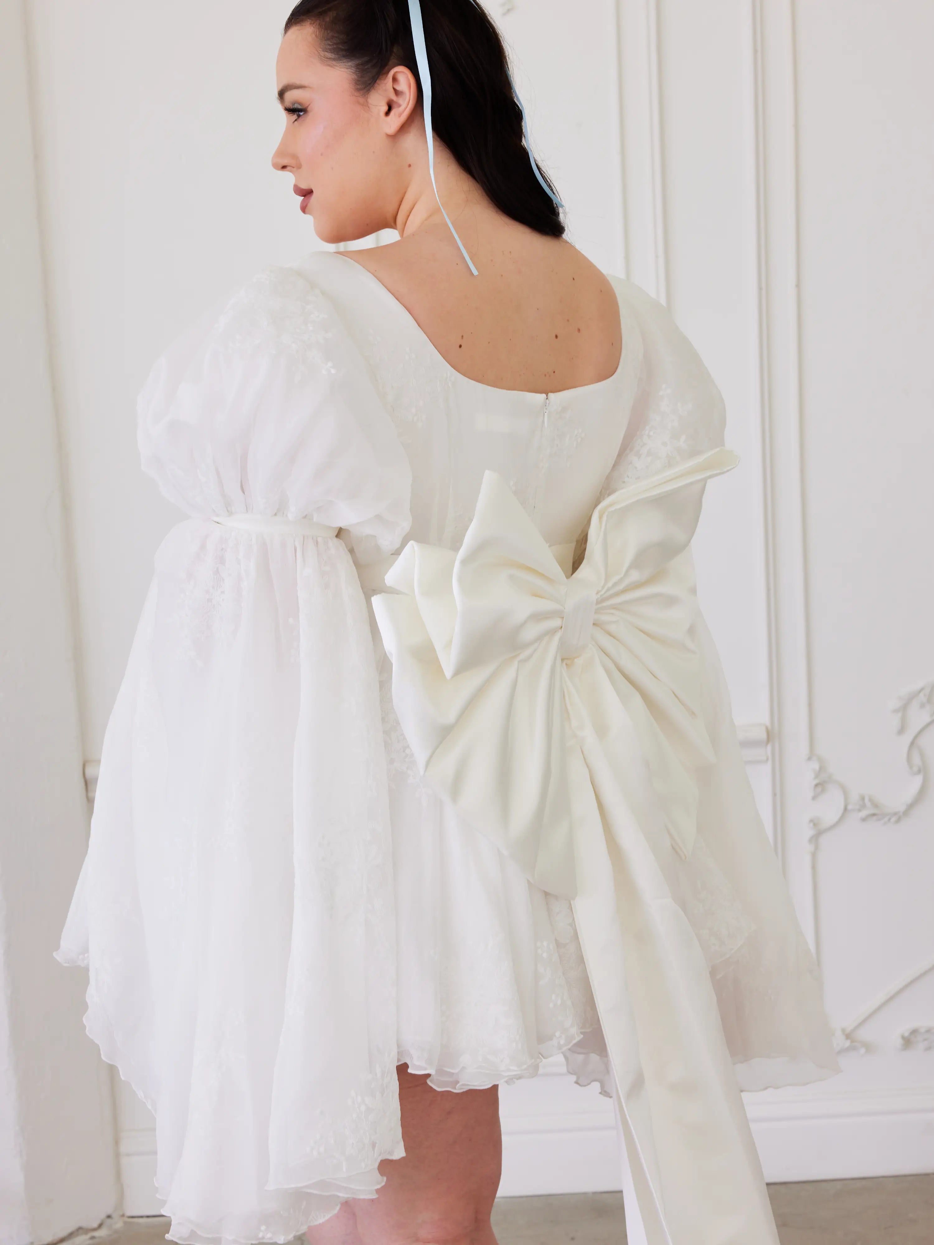 White dress with a grand bow sash and flared sleeves exuding whimsical elegance