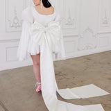 White wedding dress with long train and bell sleeves showcasing whimsical elegance and Grand Bow Sash