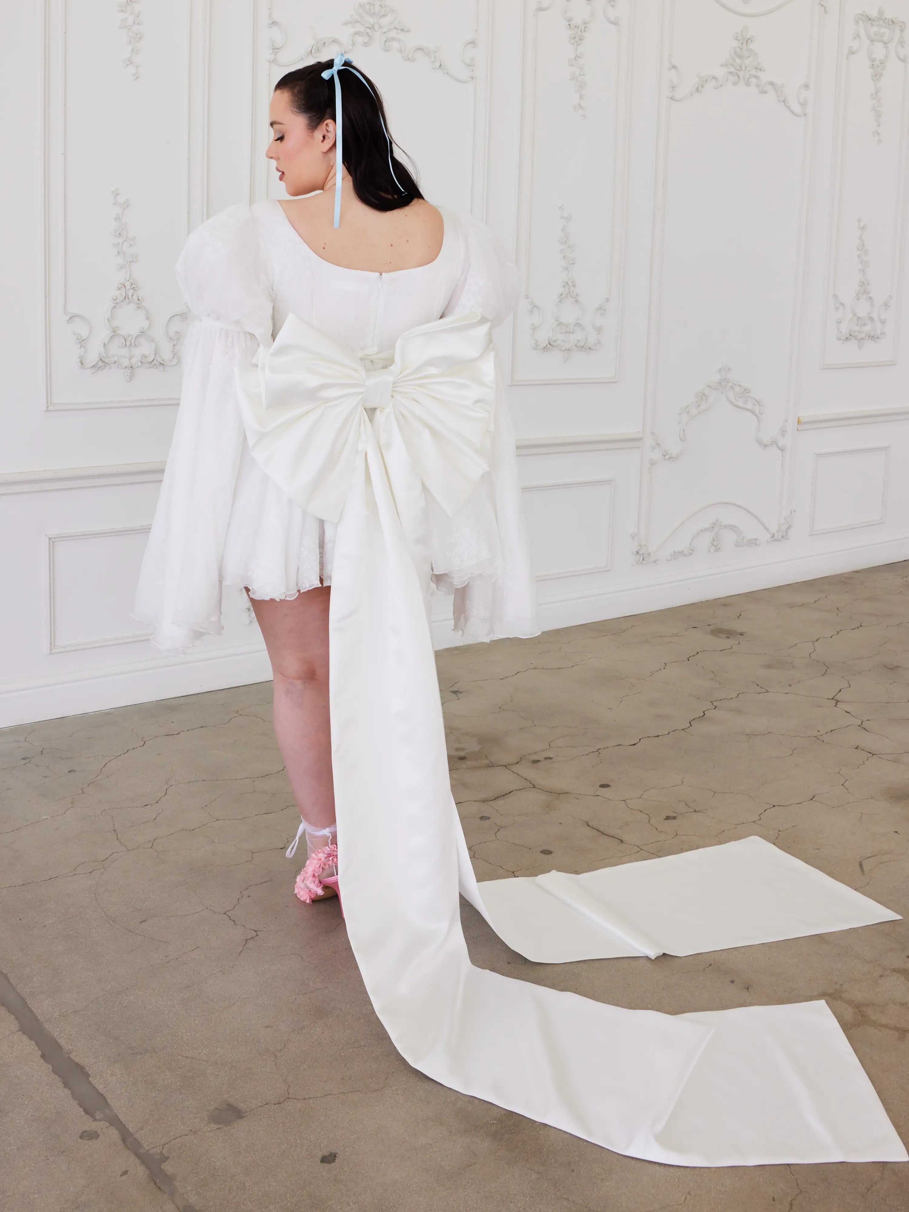 White wedding dress with long train and bell sleeves showcasing whimsical elegance and Grand Bow Sash