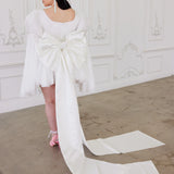 Woman showcasing whimsical elegance in The Ivory Grand Bow Sash with a long trailing bow