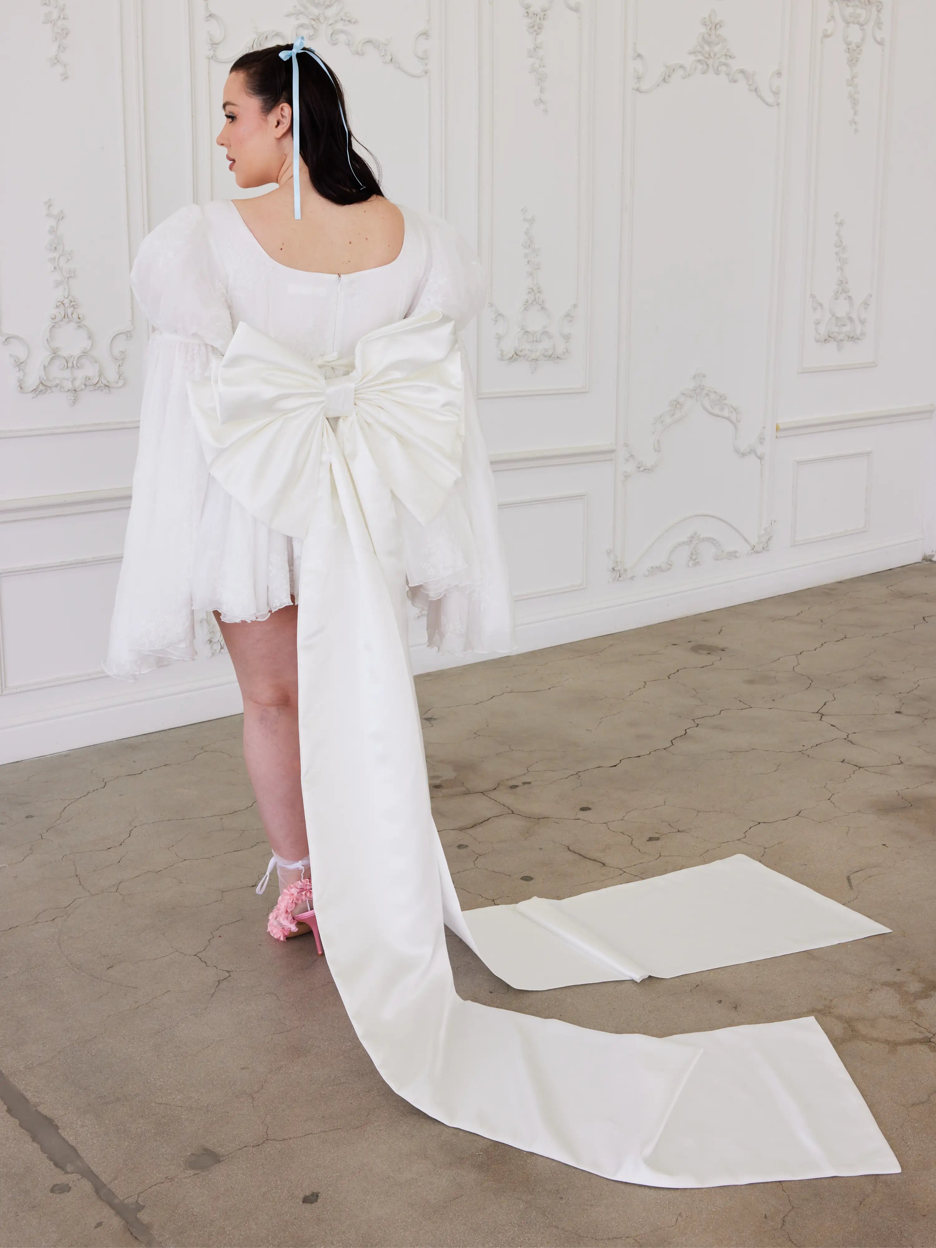 Woman showcasing whimsical elegance in The Ivory Grand Bow Sash with a long trailing bow