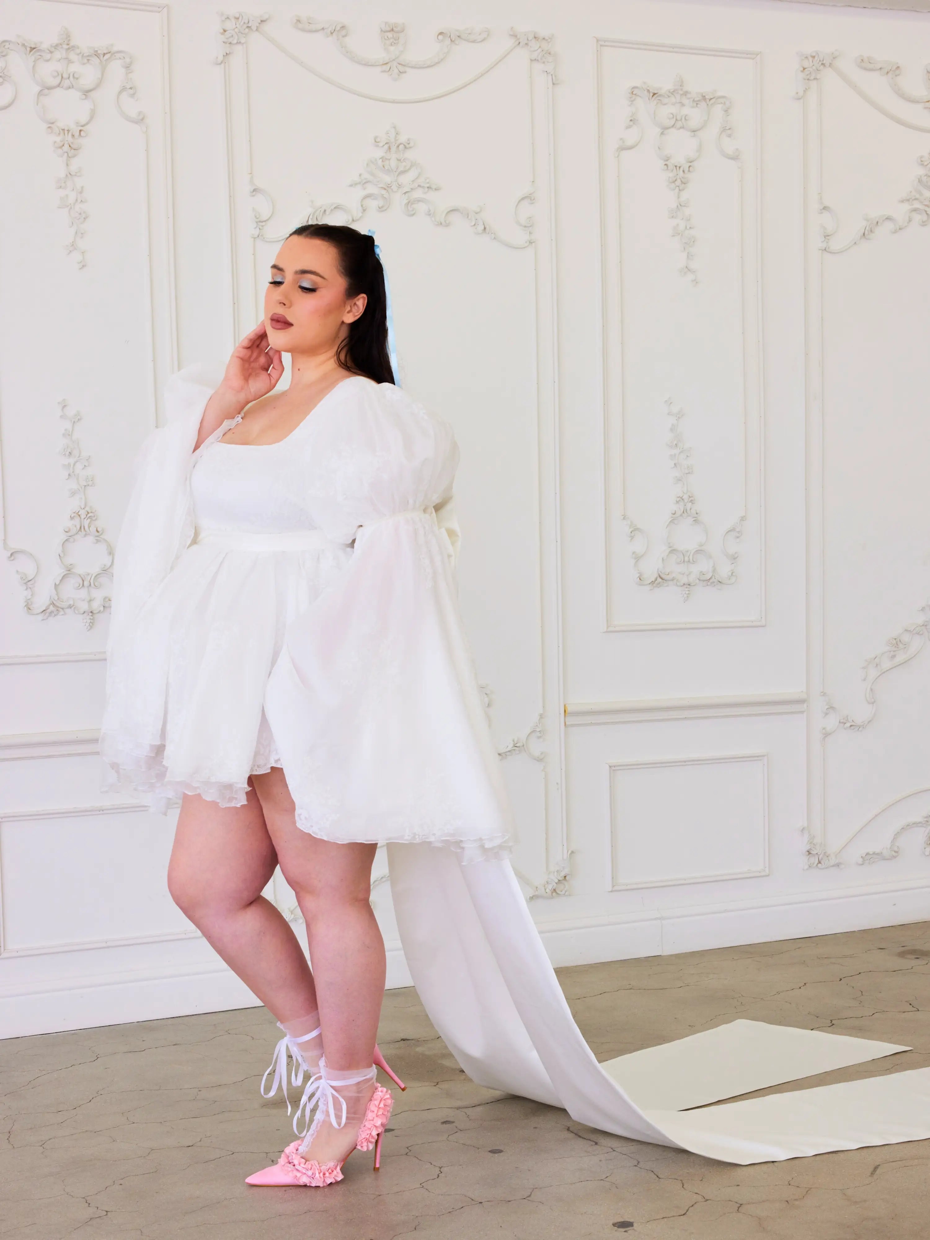 Woman in a white dress with a long train and pink heels, showcasing Whimsical Elegance of The Ivory Grand Bow Sash