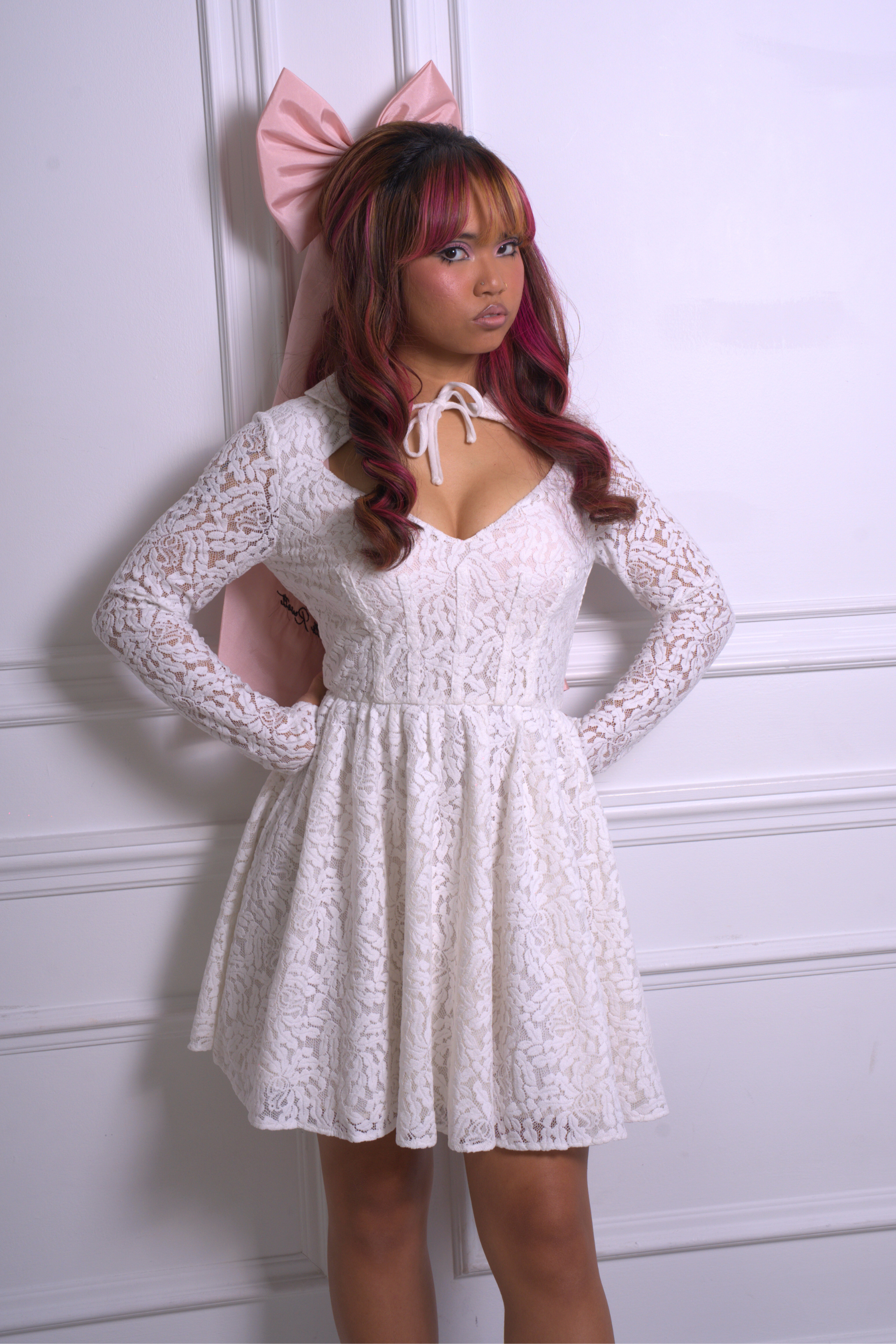 A woman wearing Ivory Sheep's Dolls Revolt Pink Hair Bow paired with a white lace dress against a white wall.