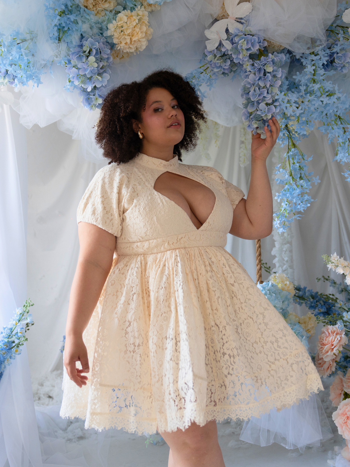 A woman in Ivory Sheep's Victorian Lace Mini Dress for the Dresses & Gowns collection is standing in front of floral decorations