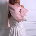 A woman wearing Ivory Sheep's Eloise Lace Mini Dress with a pink hairbow, reading "the dolls revolt" against a white wall.